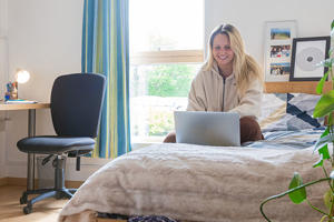 a smiling student is sitting on a bed in  accommodation