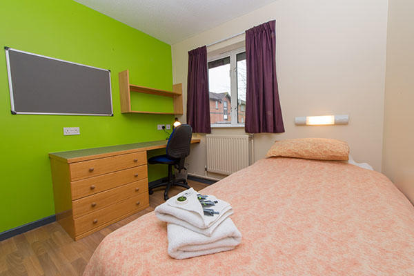 A bedroom inside  accommodation. There is a single bed, a large pin board, desk, chest of drawers and a window in the room.
